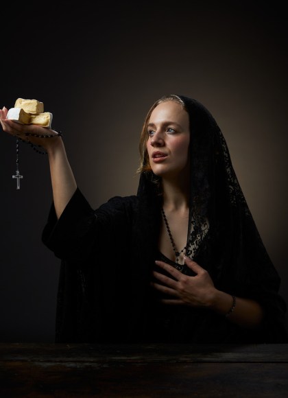 Photo of author Erika Kubick in a long black veil gazing in divine wonder at the sacred cheese cubes she holds in her hand. A rosary also dangles from the same hand.